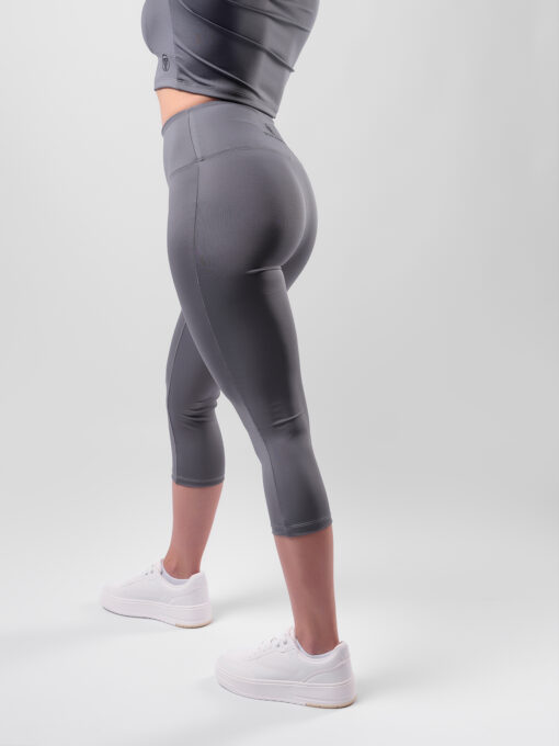 Dámske Capri legíny – Titanium Grey – STAY POSITIVE® Nechajte sa rozmaznávať materiálom, ktorý bol vybraný pre vaše maximálne pohodlie a dokonalý vzhľad! Tieto dámske legíny sú šité v strihu bez predného švíku medzi nohami, vysoký dvojmo šitý pás dokonale formuje postavu, drží na mieste a nešmýka sa.